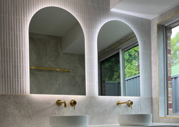 Modern bathroom with arched mirrors and gold fixtures.
