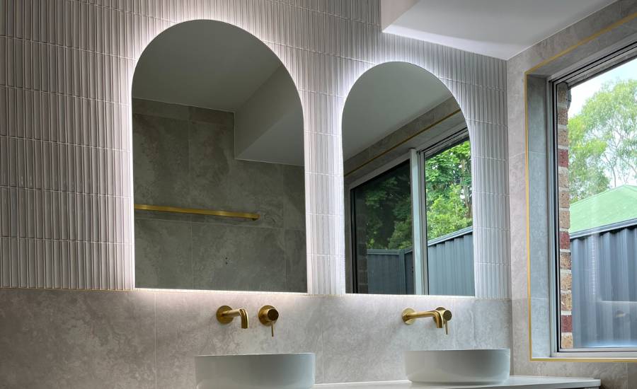 Modern bathroom with arched mirrors and gold fixtures.