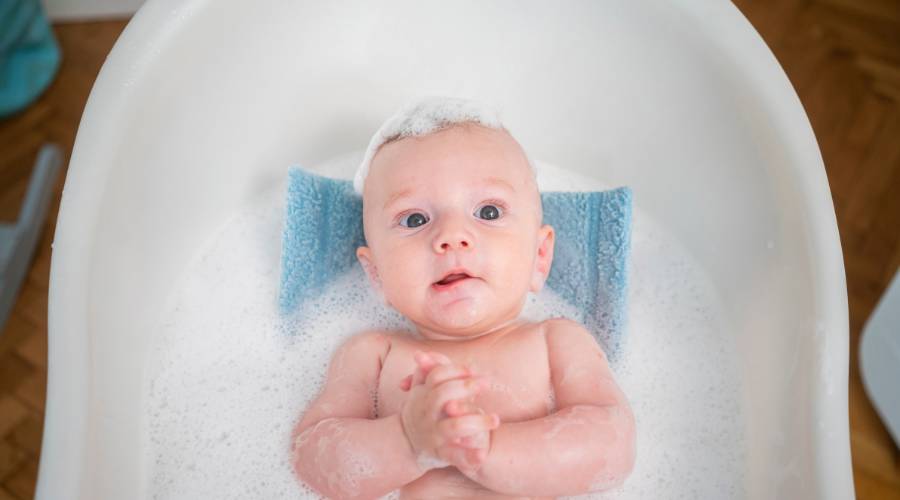Baby in bathtub with bubbles and towel.