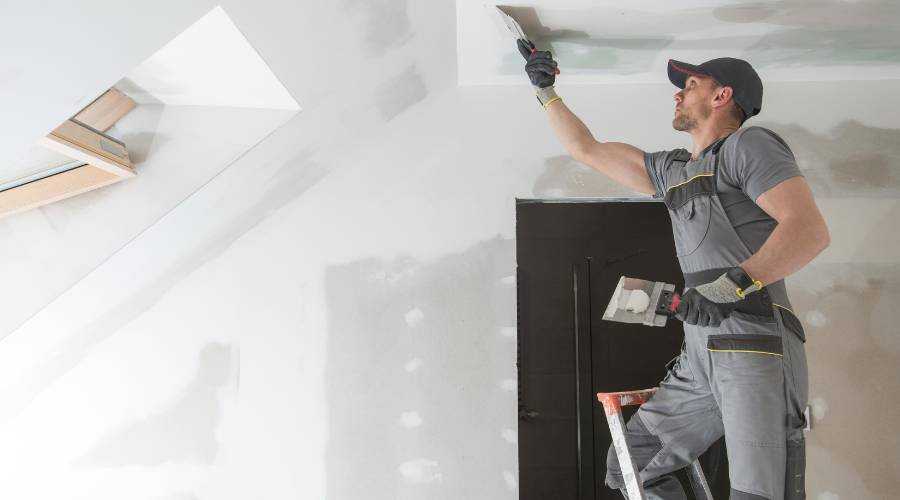 Worker plastering ceiling on a ladder