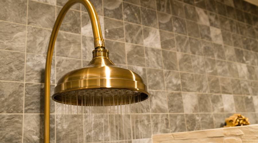 Gold shower head with gray tiled wall