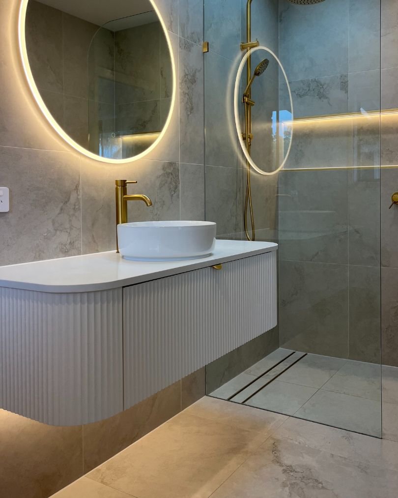 Modern bathroom with gold fixtures and round mirrors.