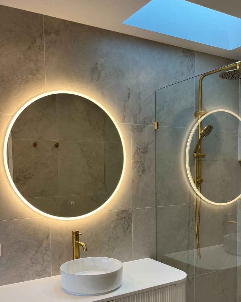 Modern bathroom with illuminated round mirror and fixtures.