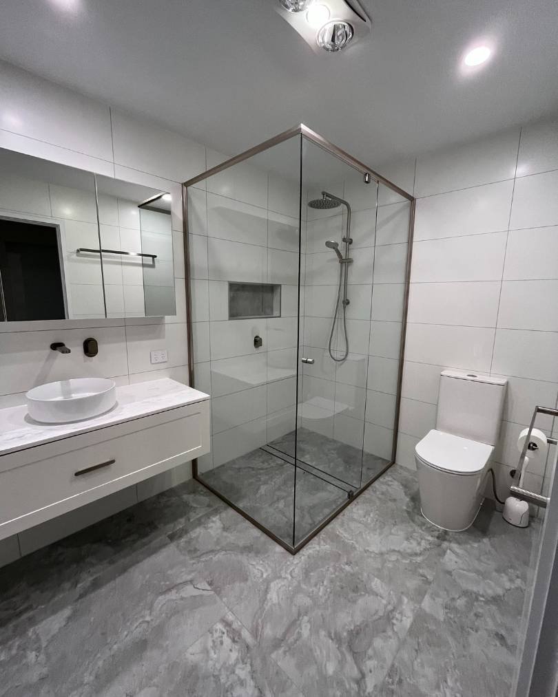 Modern bathroom with glass shower and gray tiles.
