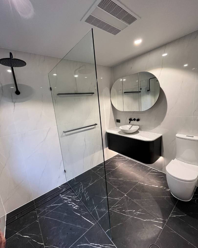 Modern bathroom with glass shower and black accents.